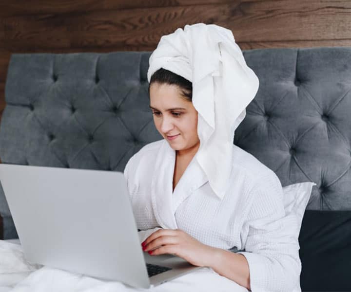 a woman sitting on her bed in a bath robe browsing the web