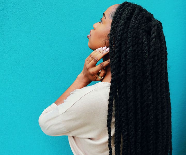 woman with long crochet braids holding neck staring at wall