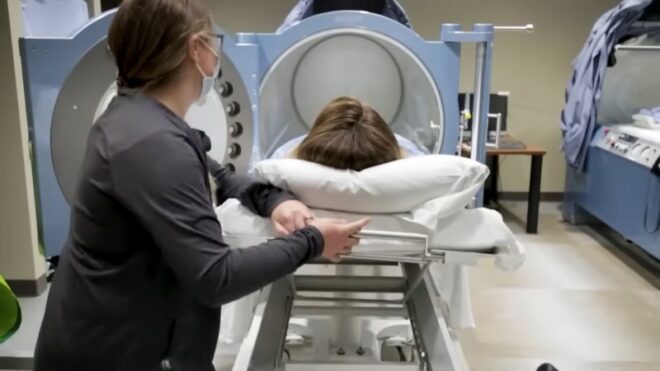 A patient is guided into a hyperbaric chamber by a healthcare worker during treatment setup