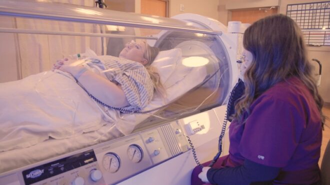 A patient in a hyperbaric oxygen chamber monitored by a medical professional for safety