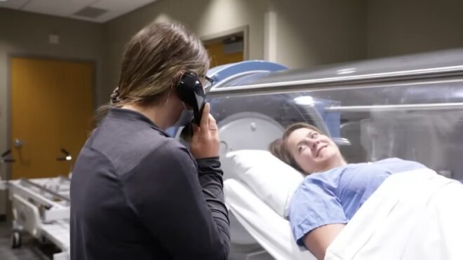 A patient inside a hyperbaric chamber talks with a medical staff member through the intercom