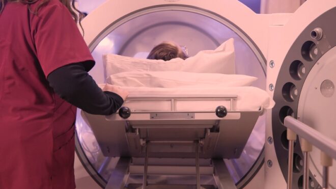 A patient being slid into a hyperbaric oxygen therapy chamber by a medical staff member